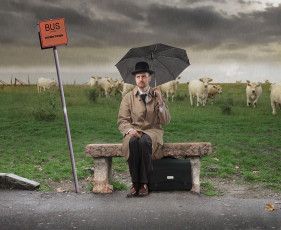 عکس مرد با چتر و کلاه در ایستگاه اتوبوس کنار مزرعه